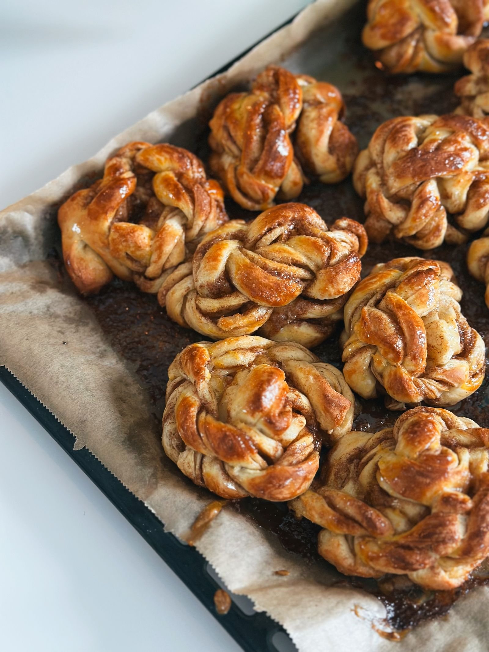 Glazed hand-tied cinnamon knots on a parchment-lined baking tray