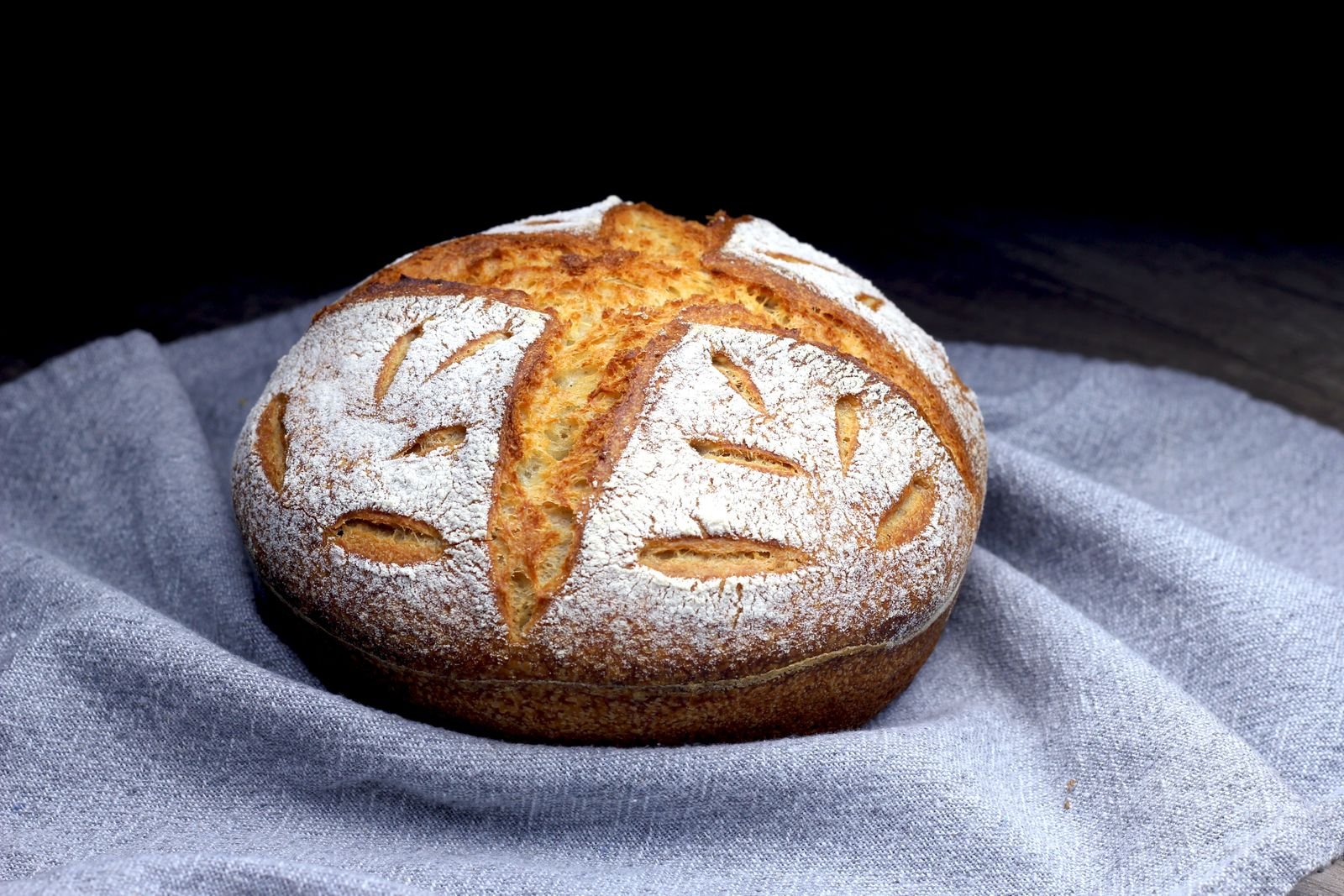 Flour-dusted round sourdough boule with leaf-pattern scoring on a linen cloth