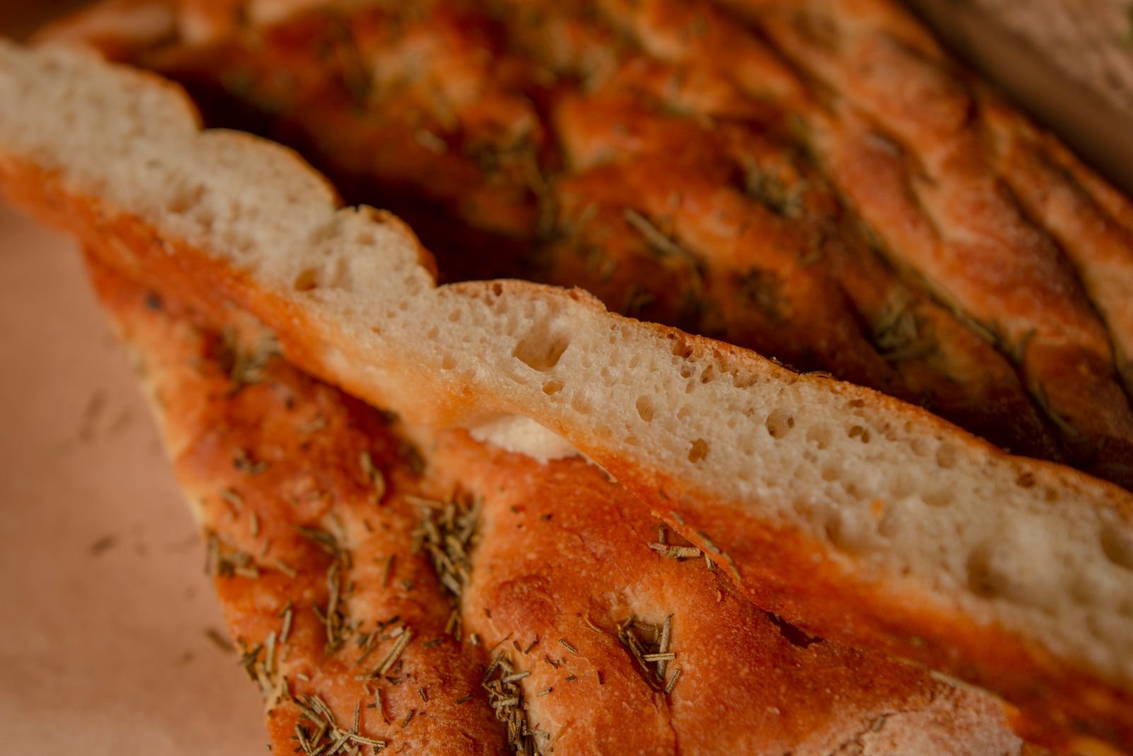 Golden rosemary focaccia cut into slices, glossy with olive oil