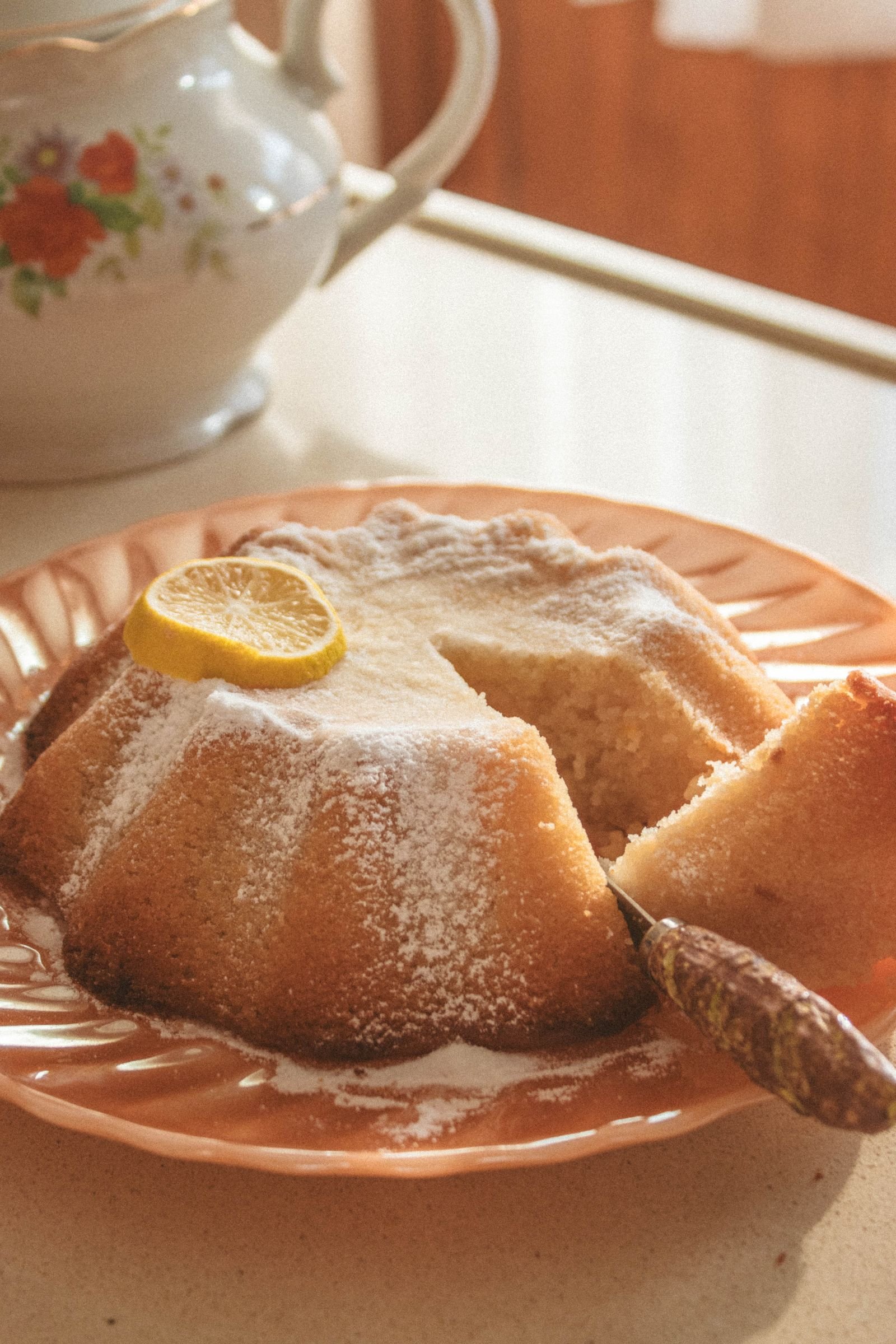 Homemade lemon cake dusted with icing sugar, one slice cut